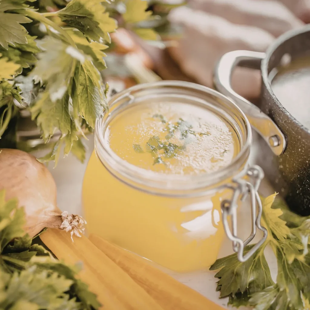 Pote de vidro com caldo translúcido de vegetais e ervas frescas