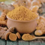 Raízes de cúrcuma frescas e pó de cor laranja vibrante em uma colher