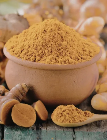 Raízes de cúrcuma frescas e pó de cor laranja vibrante em uma colher