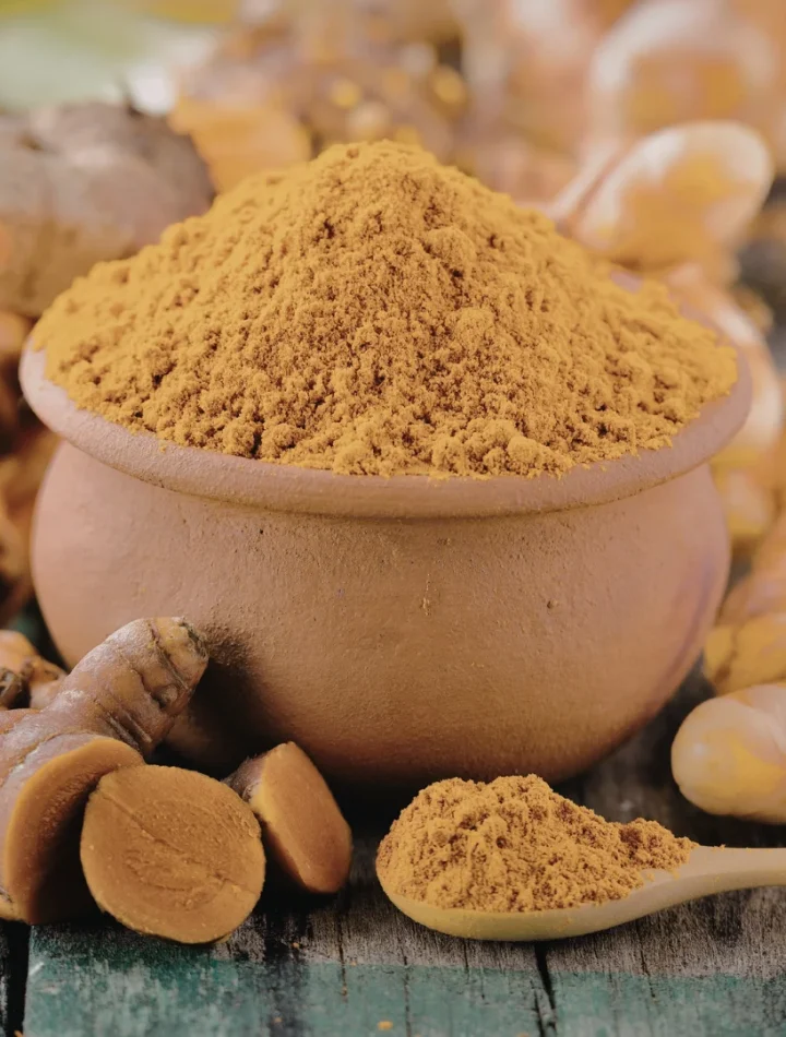 Raízes de cúrcuma frescas e pó de cor laranja vibrante em uma colher